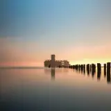 Wschód słońca Gdynia. Betonowa forteca na wodzie, drewniane pale tworzą ścieżkę ku horyzontowi.