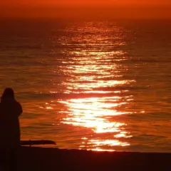 Zachód słońca w Ustce. Samotna postać na plaży podziwia złocistą ścieżkę na morzu.