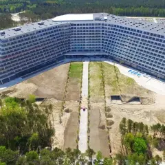 Nowoczesny hotel Gołębiewski w Pobierowie, z tarasami i basenem, otoczony lasem i placem budowy.