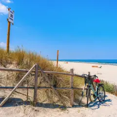 Rower czeka przy płocie na plaży, gotowy do odkrywania tras rowerowych nad morzem. W tle błękitne niebo i morze.