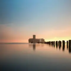 Wschód słońca Gdynia. Betonowa forteca na wodzie, drewniane pale tworzą ścieżkę ku horyzontowi.