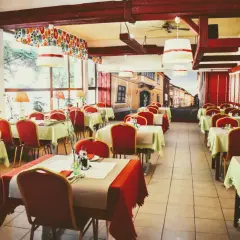 Wnętrze restauracji z czerwonymi krzesłami i stolikami nakrytymi na przyjęcie. Mural z ulicą przypomina czardasz Gdańsk.