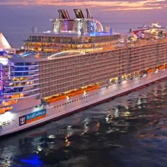 Ogromny statek wycieczkowy Royal Caribbean lśni w blasku zachodzącego słońca, z kolorowymi światłami i zjeżdżalniami wodnymi.