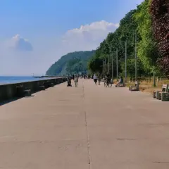 Spacerowicze i rowerzyści cieszą się słonecznym dniem na bulwarze w Gdyni. W tle widać morze i zielone wzgórza.