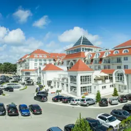 Elegancki hotel 5 gwiazdkowy nad morzem z przestronnym parkingiem pełnym samochodów.
