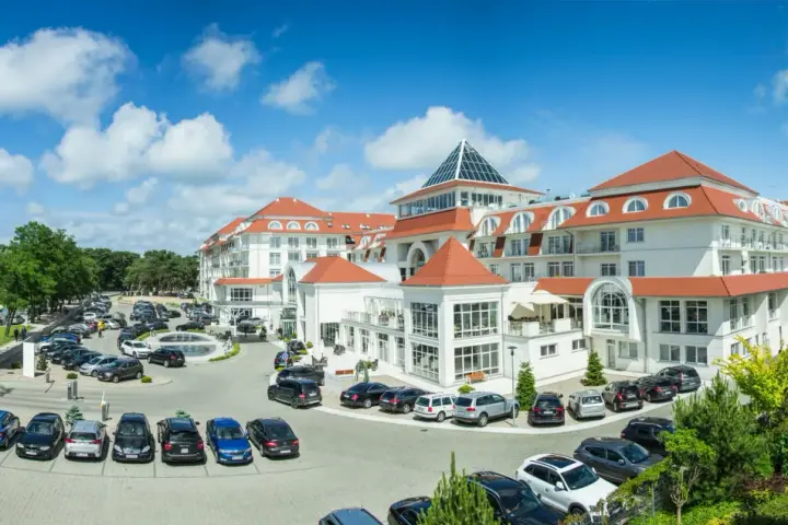 Elegancki hotel 5 gwiazdkowy nad morzem z przestronnym parkingiem pełnym samochodów.
