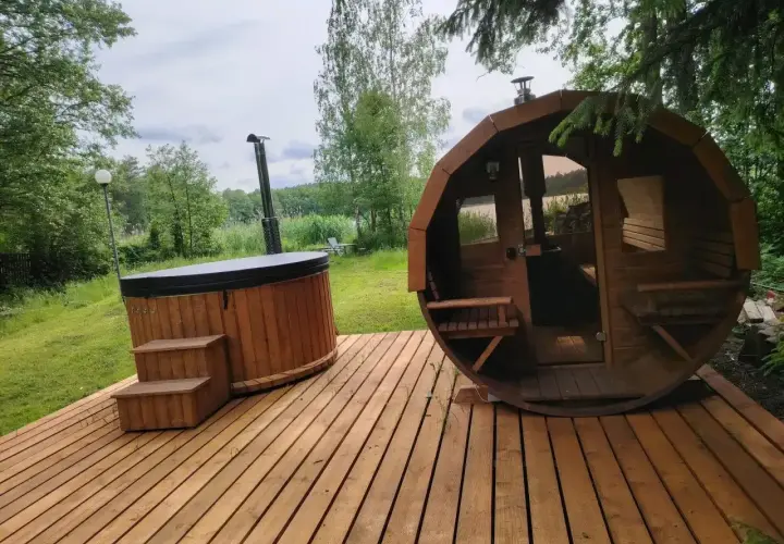 Drewniany domek z jacuzzi i sauną na wyłączność, otoczony zielenią, z widokiem na jezioro. Idealne miejsce na relaks.