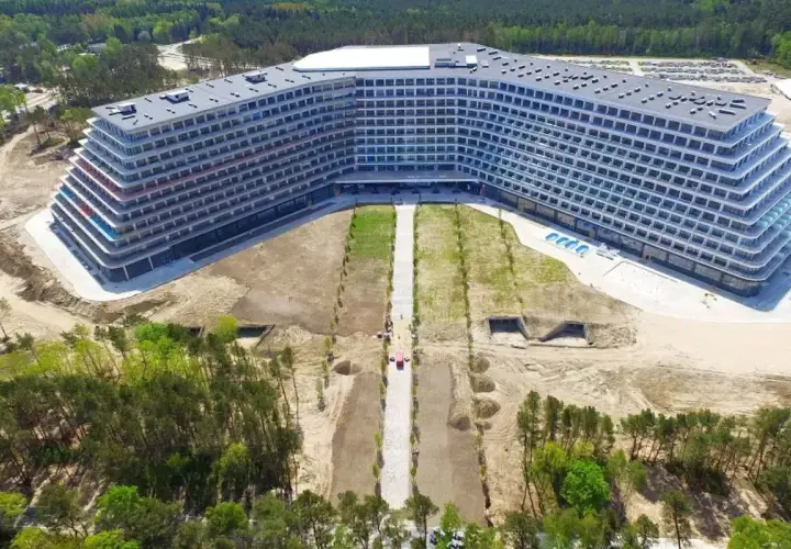 Nowoczesny hotel Gołębiewski w Pobierowie, z tarasami i basenem, otoczony lasem i placem budowy.