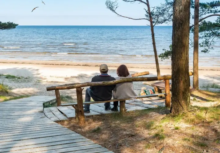 Para odpoczywa na ławce przy plaży, ciesząc się widokiem morza. Idealne miejsce na regenerację w sanatorium nad morzem.