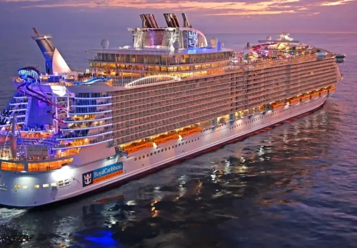 Ogromny statek wycieczkowy Royal Caribbean lśni w blasku zachodzącego słońca, z kolorowymi światłami i zjeżdżalniami wodnymi.