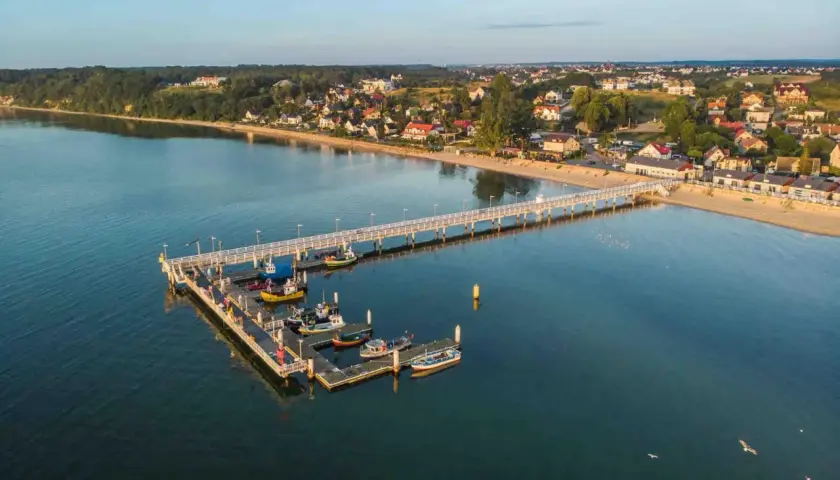 Molo w Mechelinkach z łodziami i widokiem na plażę i zabudowania. Idealne miejsce na spacer i podziwianie atrakcji.