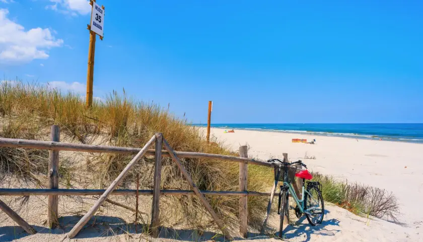 Rower czeka przy płocie na plaży, gotowy do odkrywania tras rowerowych nad morzem. W tle błękitne niebo i morze.