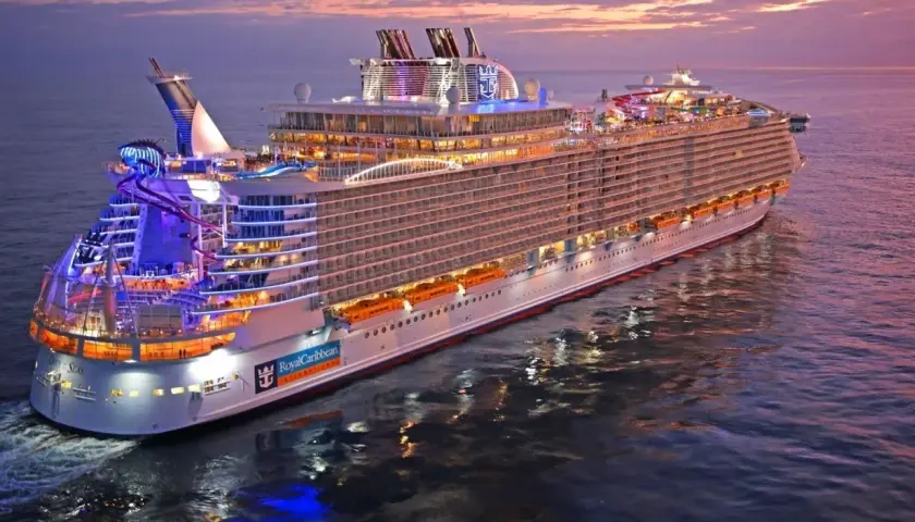 Ogromny statek wycieczkowy Royal Caribbean lśni w blasku zachodzącego słońca, z kolorowymi światłami i zjeżdżalniami wodnymi.