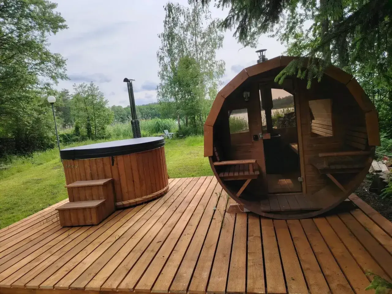 Drewniany domek z jacuzzi i sauną na wyłączność, otoczony zielenią, z widokiem na jezioro. Idealne miejsce na relaks.