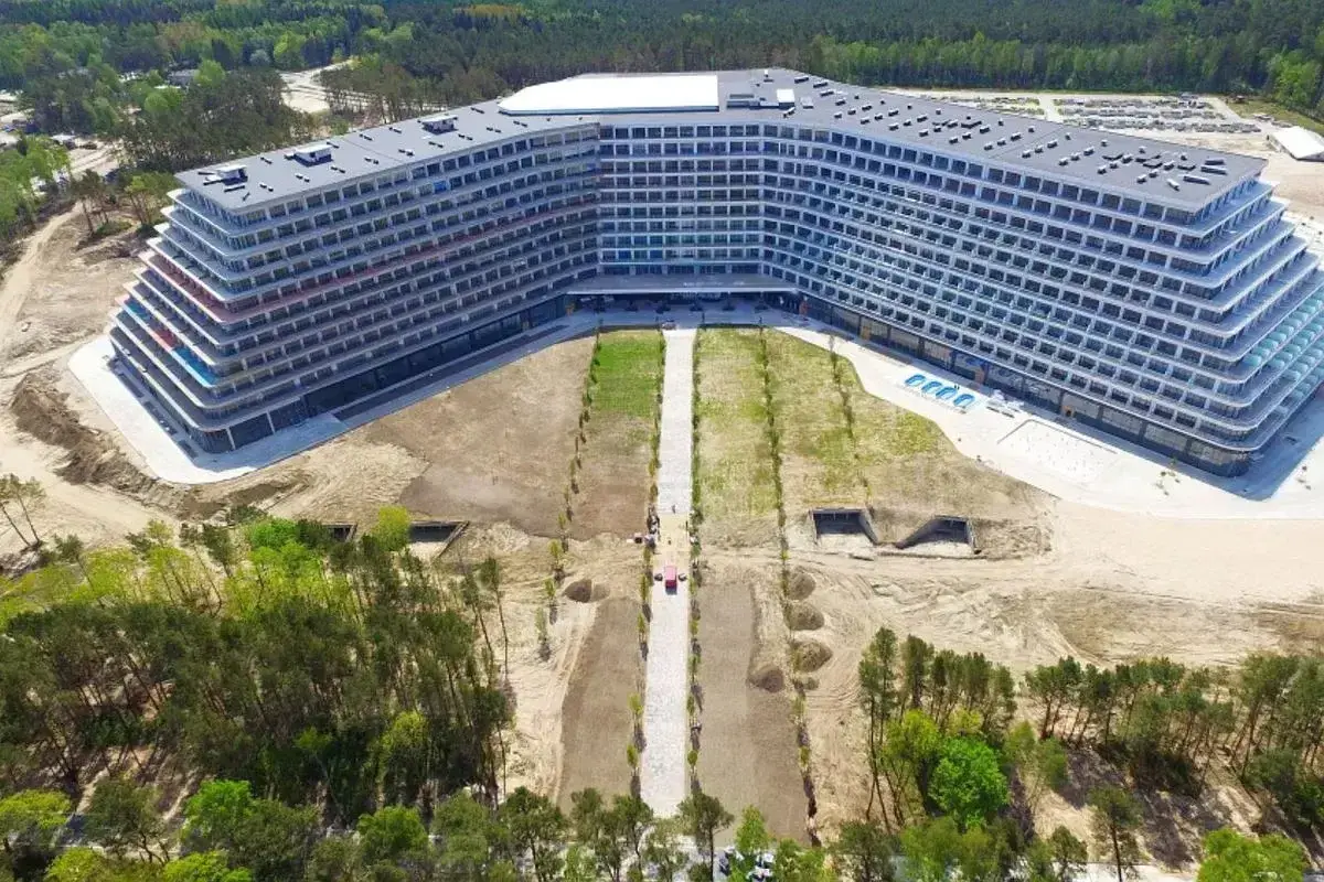 Nowoczesny hotel Gołębiewski w Pobierowie, z tarasami i basenem, otoczony lasem i placem budowy.