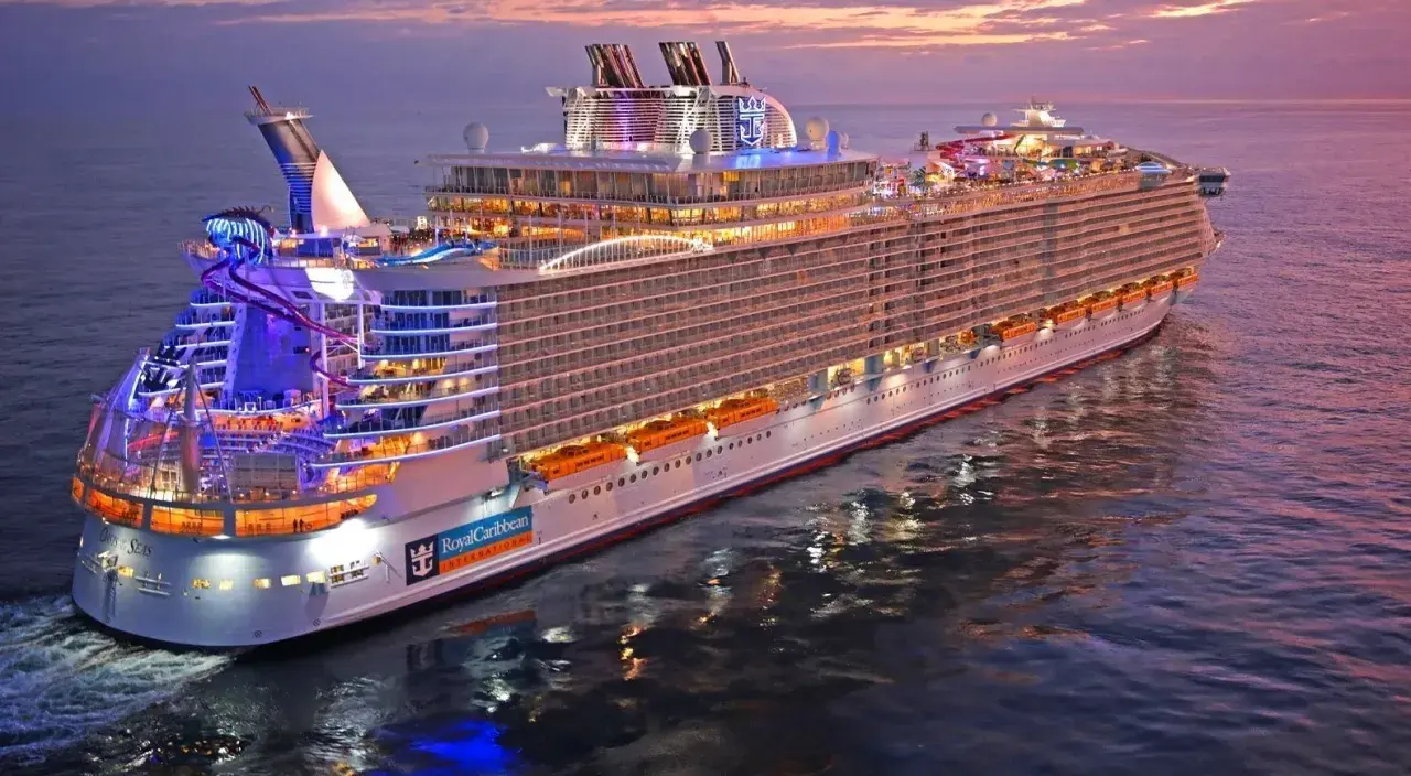 Ogromny statek wycieczkowy Royal Caribbean lśni w blasku zachodzącego słońca, z kolorowymi światłami i zjeżdżalniami wodnymi.