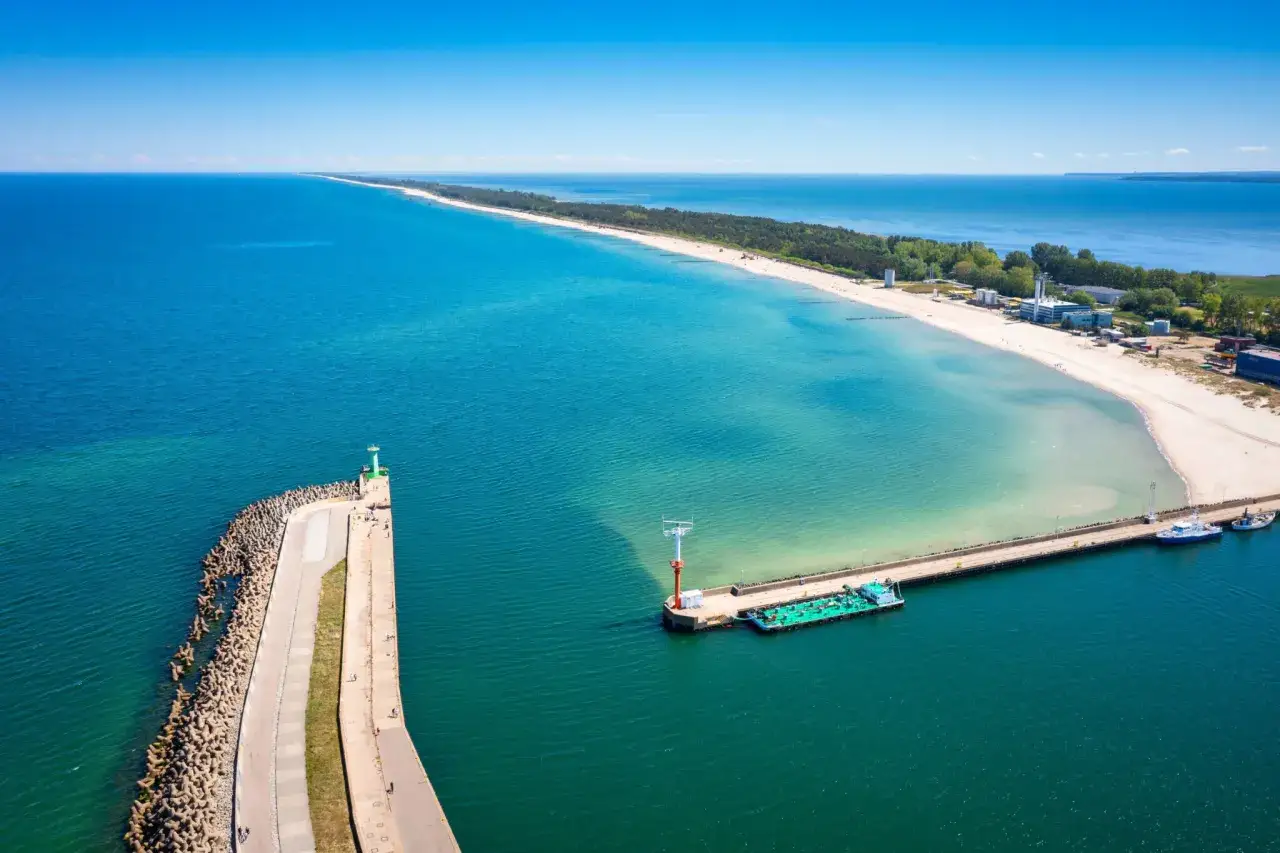 Władysławowo kamera port: widok z lotu ptaka na falochron, morze i piaszczystą plażę z budynkami w tle.
