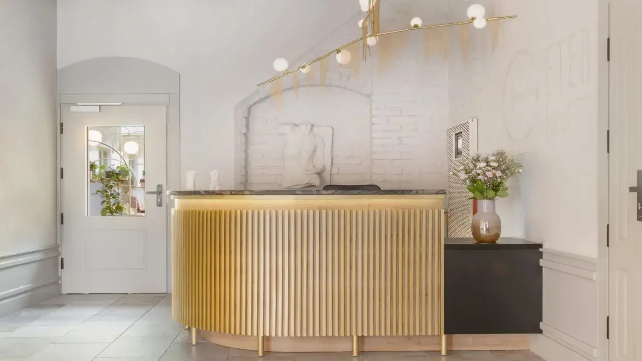 Eleganckie lobby hotelowe z ladą recepcyjną. W tle biała cegła i logo hotelu. Czas na check-in!