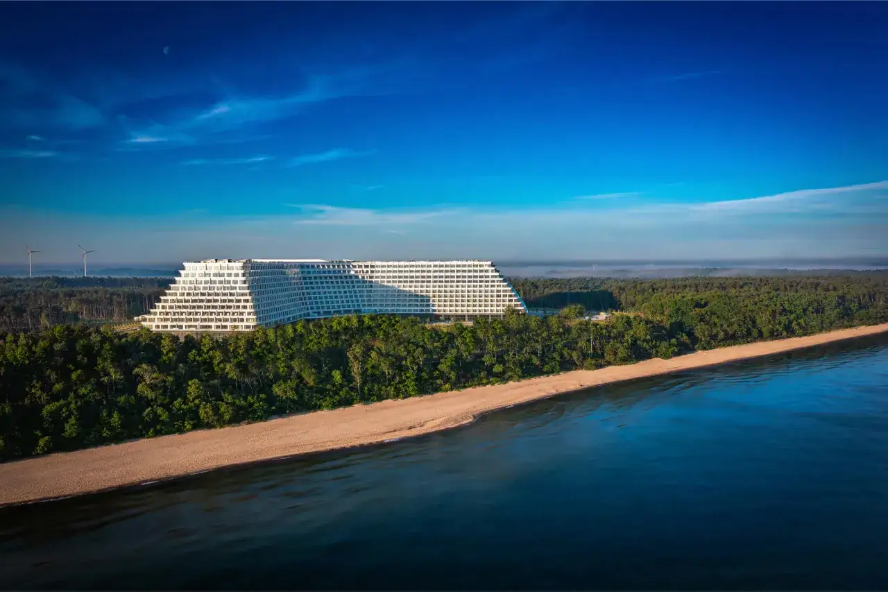 Majestatyczny hotel Gołębiewski w Pobierowie, otoczony zielonym lasem, góruje nad piaszczystą plażą i spokojnym morzem.