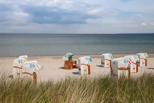 Tanie noclegi nad morzem blisko plaży. Rzędy białych koszy plażowych z numerami na piasku, morze i niebo w tle.