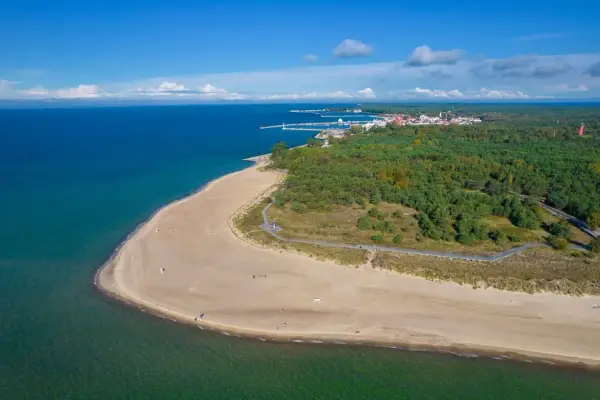 Piękny widok na plażę i las podczas rejsu Gdańsk Hel. W oddali widać zabudowania i port.